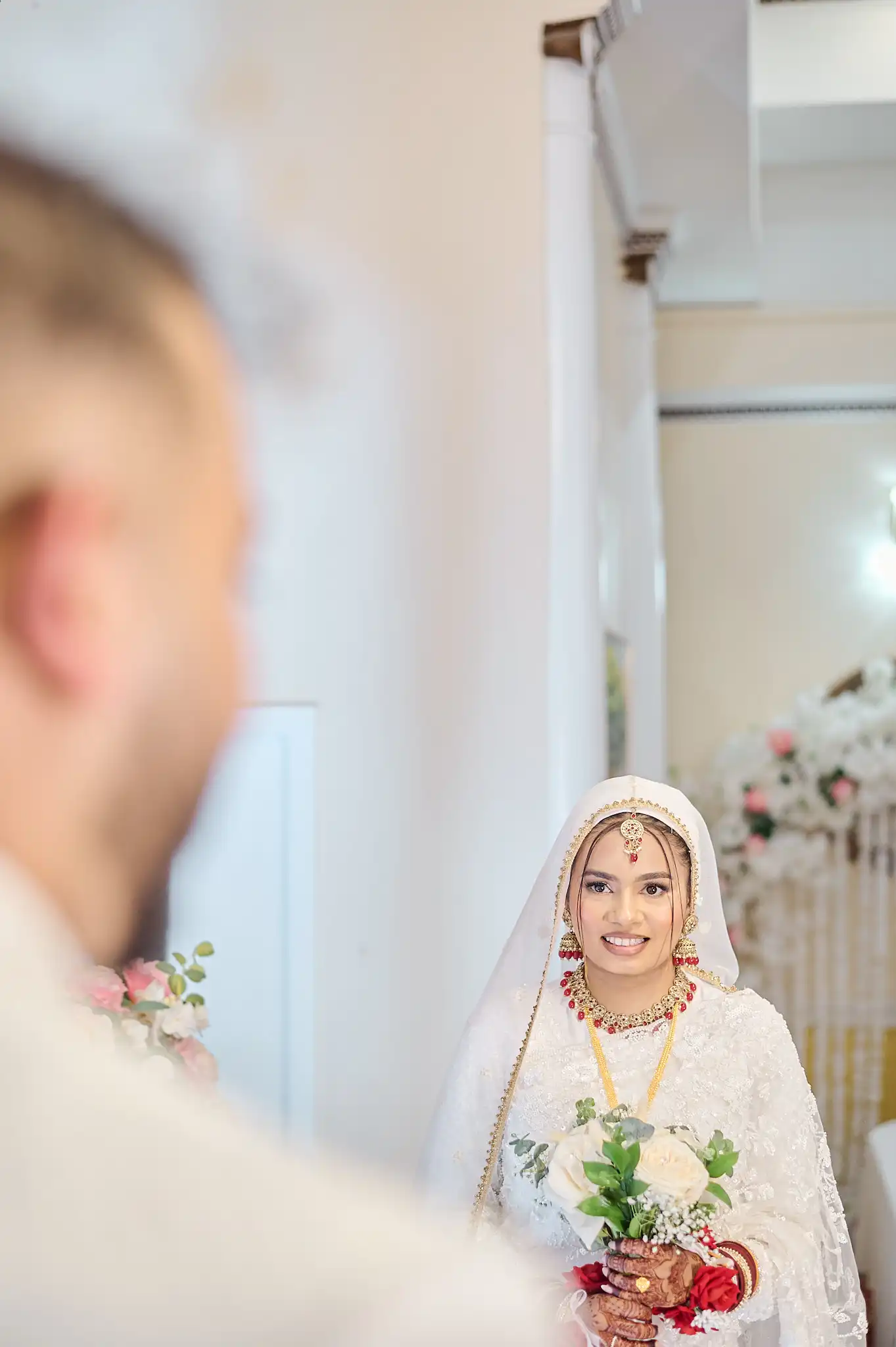 Bride in red bridal sari and groom in navy sherwani standing in front of huge brass-paneled doors
